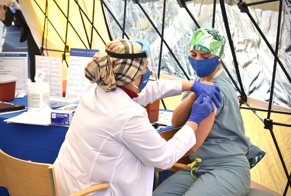 Nurse administering COVID vaccine on colleague